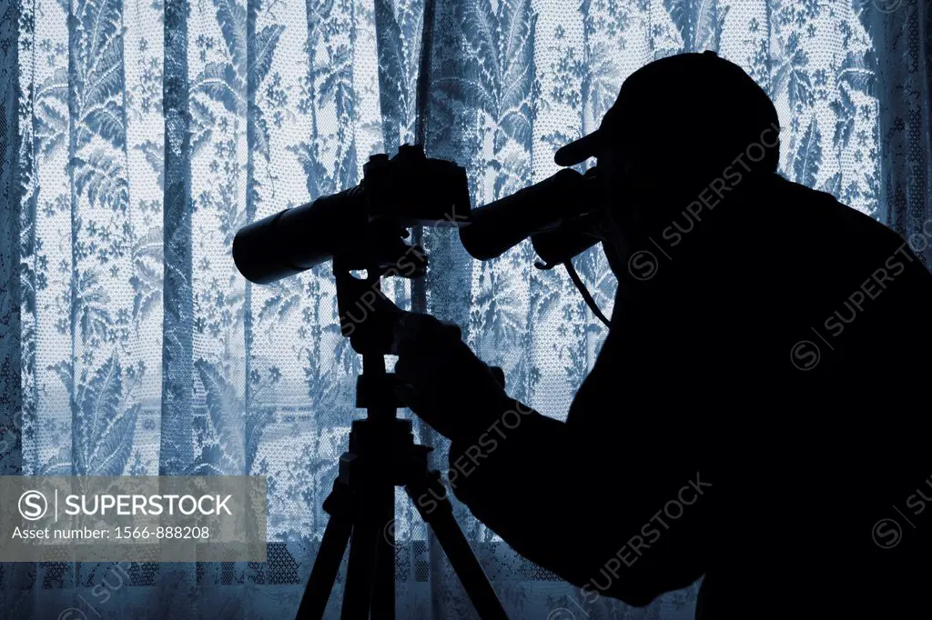Man with binoculars and camera with long lens looking out of window through net curtains  Image could be used to convey a number of themes: spying, no...