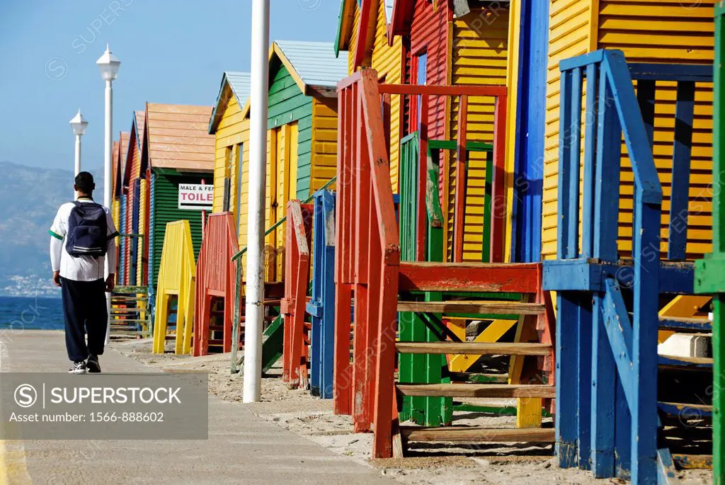 Man walking by multicoloured beach huts on Muizenberg beach, South Western Cape, South Africa