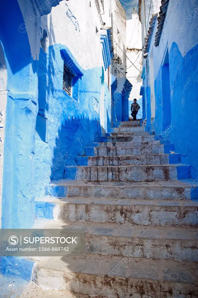 young boy coming down the stairs in one of the streets of the blue walled medina of Chefchaouen, Morocco