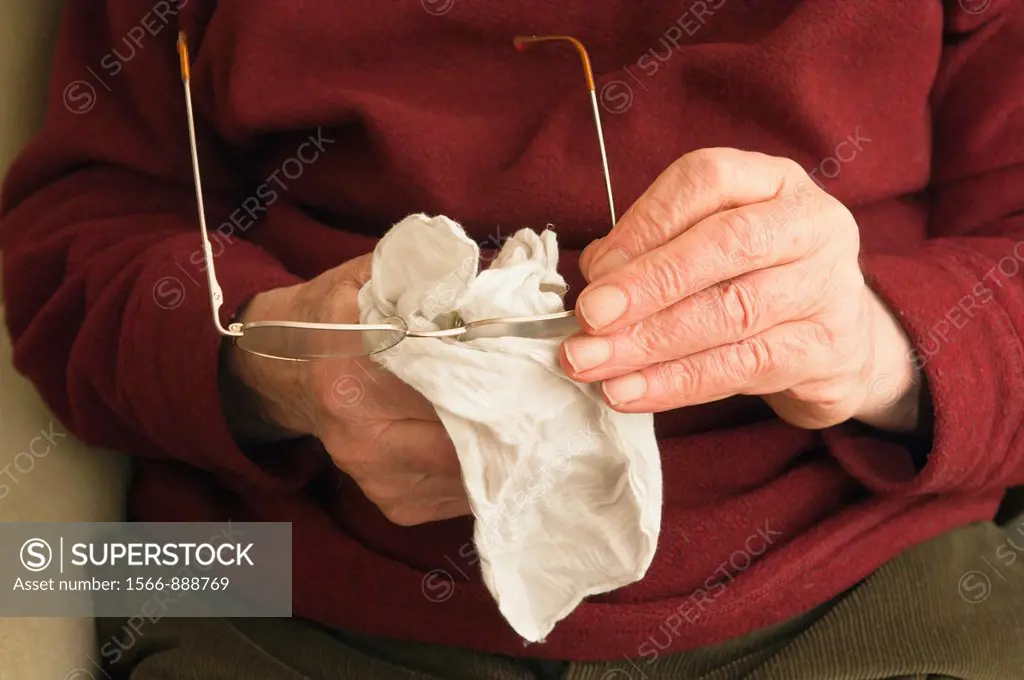 A senior elderly man in his 80´s cleaning his glasses with a hankerchief at home in England , Britain , Uk