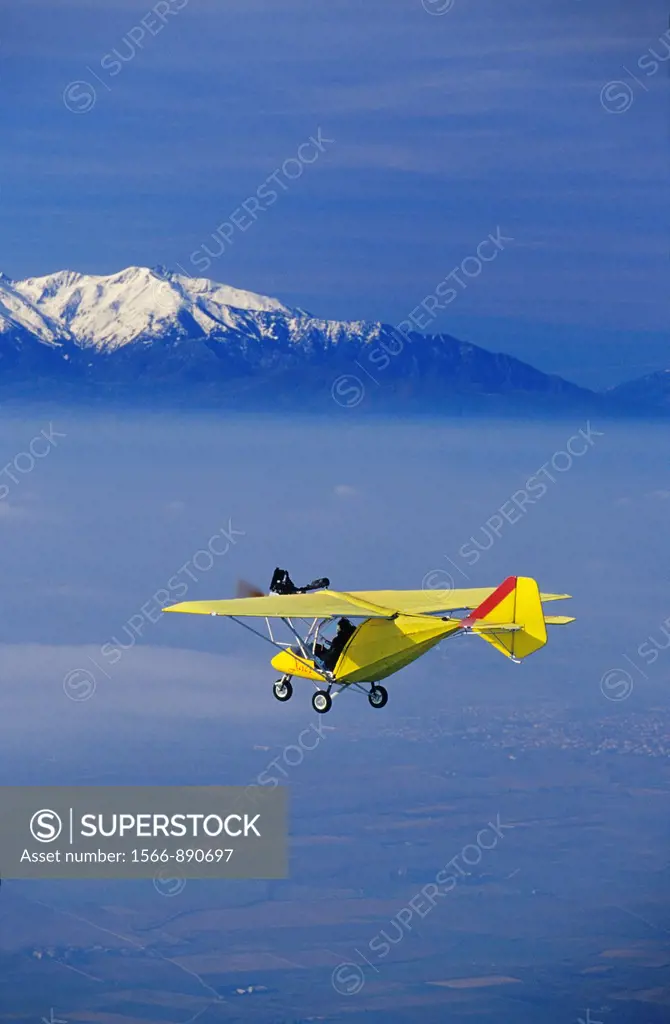 Ultra light plane flying in wintertime over thin clouds arround Torreilles  At background the snowed Canigou peak 2784 m  Orientales Pyrenees, Langued...