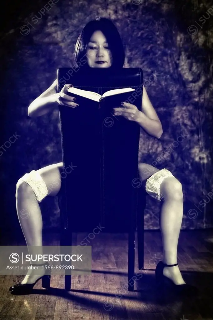 Woman sits astride a leather chair and reading a book