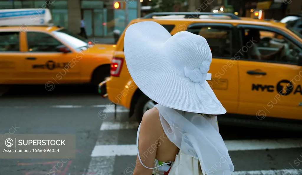 A woman wearing a big, floppy, white hat waits to cross the street in the New York neighborhood of Chelsea