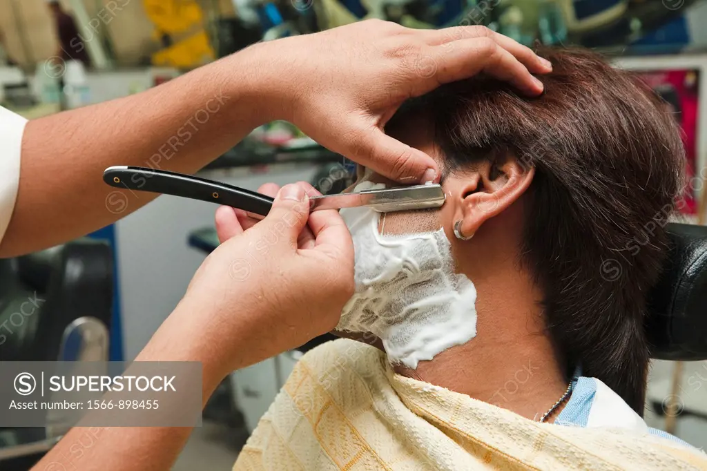 Young Arab man from Dubai getting a wet shave with an open razor in a traditional barbers shop  Old Town Souk