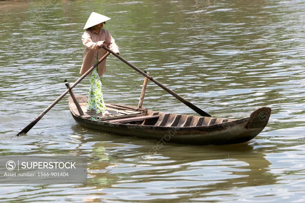 Woman in conical hat paddlling ferry boat across Mekong Delta river Vietnam