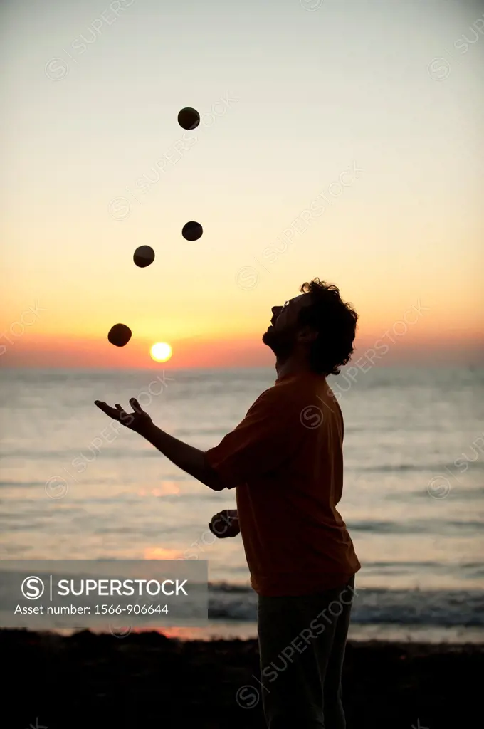 A man juggling at sunset on the beach on a very warm late september evening Aberystwyth Wales UK