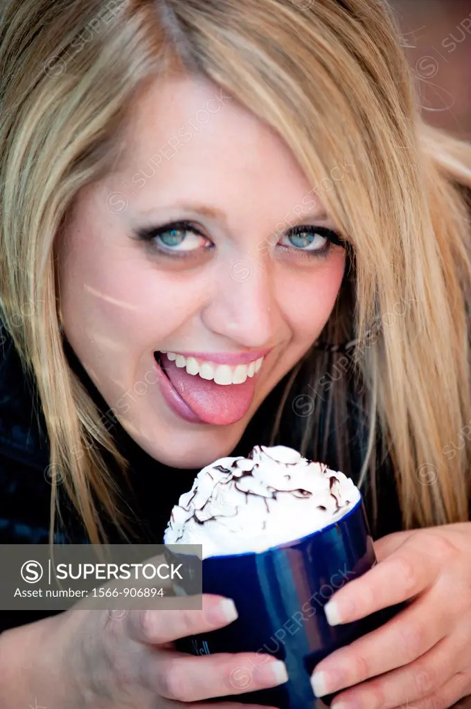 31 year old blond woman licking cream from a coffee mug in a cafe