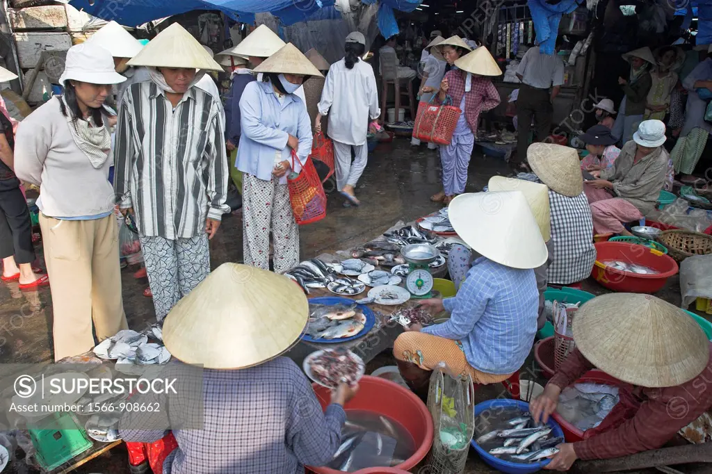 Women in conical hats buy and ssell fish at riverside market Hoi An historic town mid Vietnam