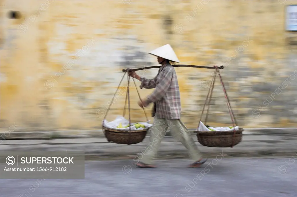 Conical hat woman with banana baskets walks from market Hoi An historic town mid Vietnam