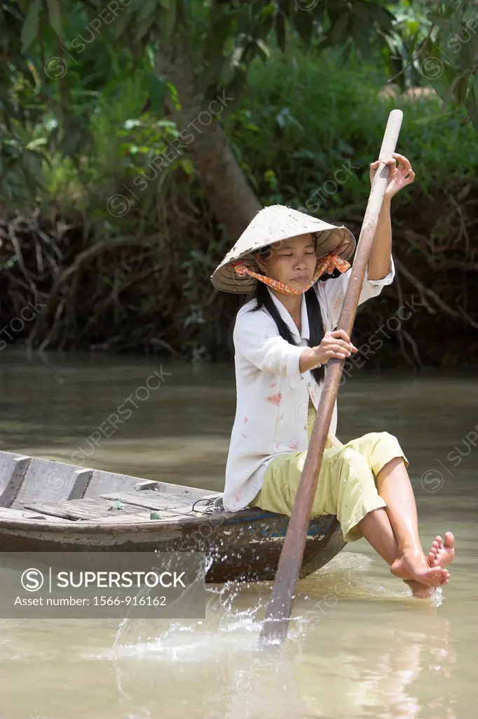 Woman in conical hat paddling boat through Mekong Delta backwaters Vietnam