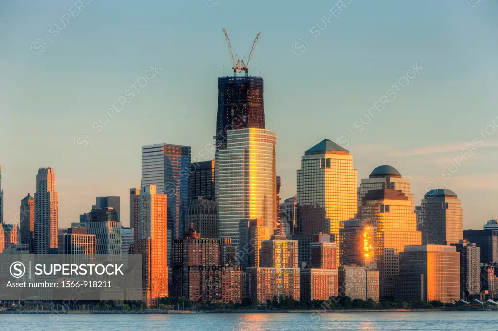 The sunset colored sky is reflected off of the building facades in lower Manhattan, including the World Financial Center and Battery Park City. The ri...