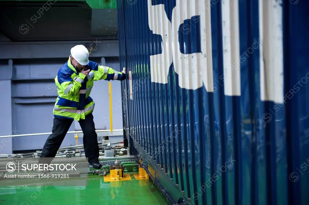 The loading Master from the docks in Sundsvall, Sweden is directing or pushing a loaded container, hanging from a crane, to it´s final position on the...