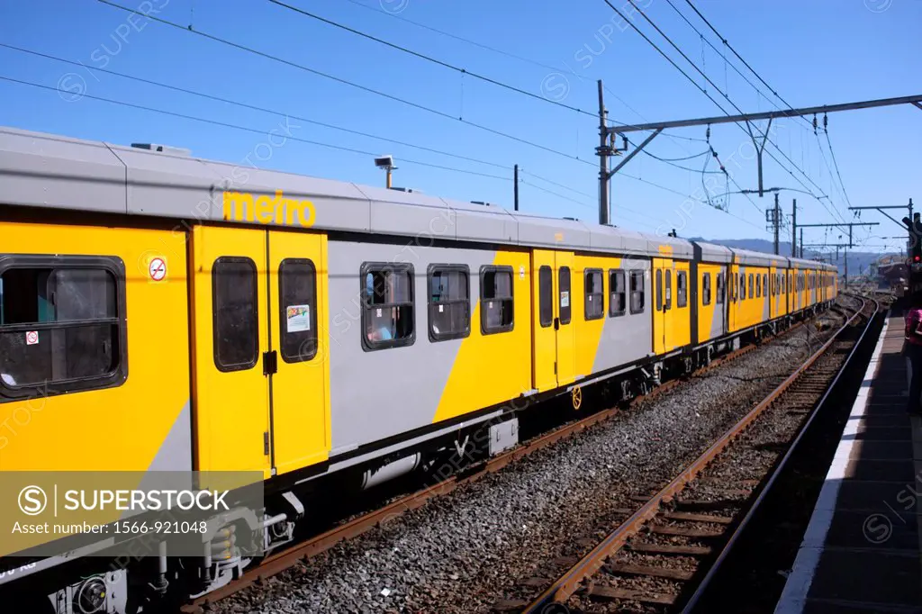 The yellow Metro of Cape Town´s mass transit system crossing at a train station, Muizenberg, False Bay, South Africa