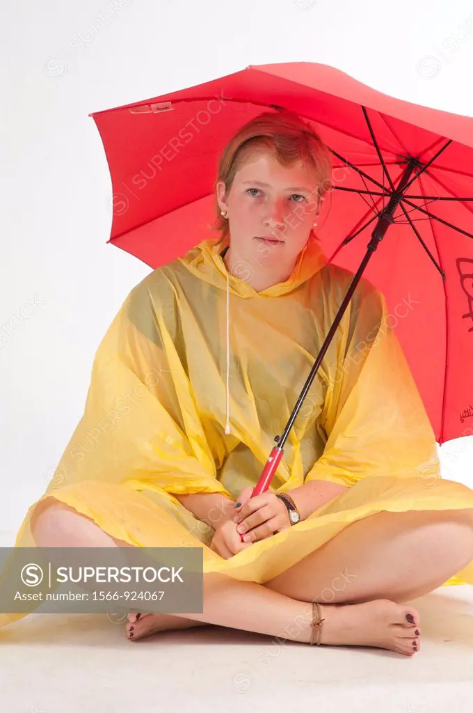 Teenage girl sitting on the floor with yellow rain gear protected with red umbrella.
