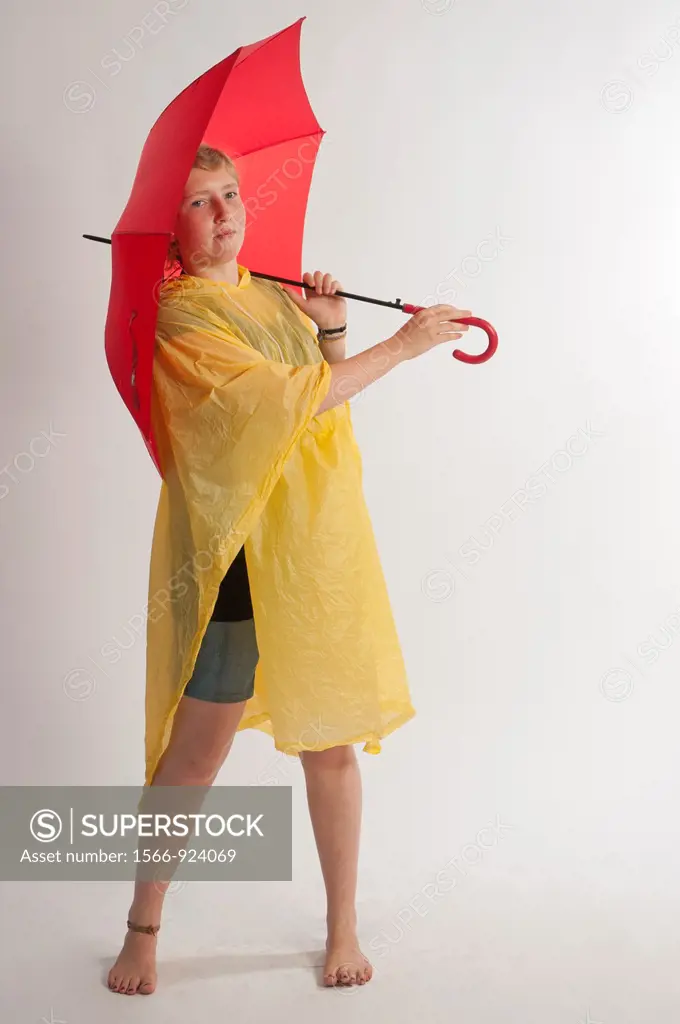 Teenage girl with yellow rain gear protected with red umbrella.