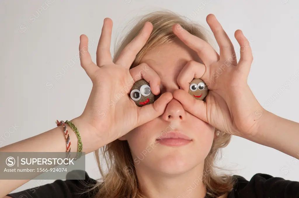 Blonde girl holding her hands in the shape of a pair of binoculars in front of her eyes.