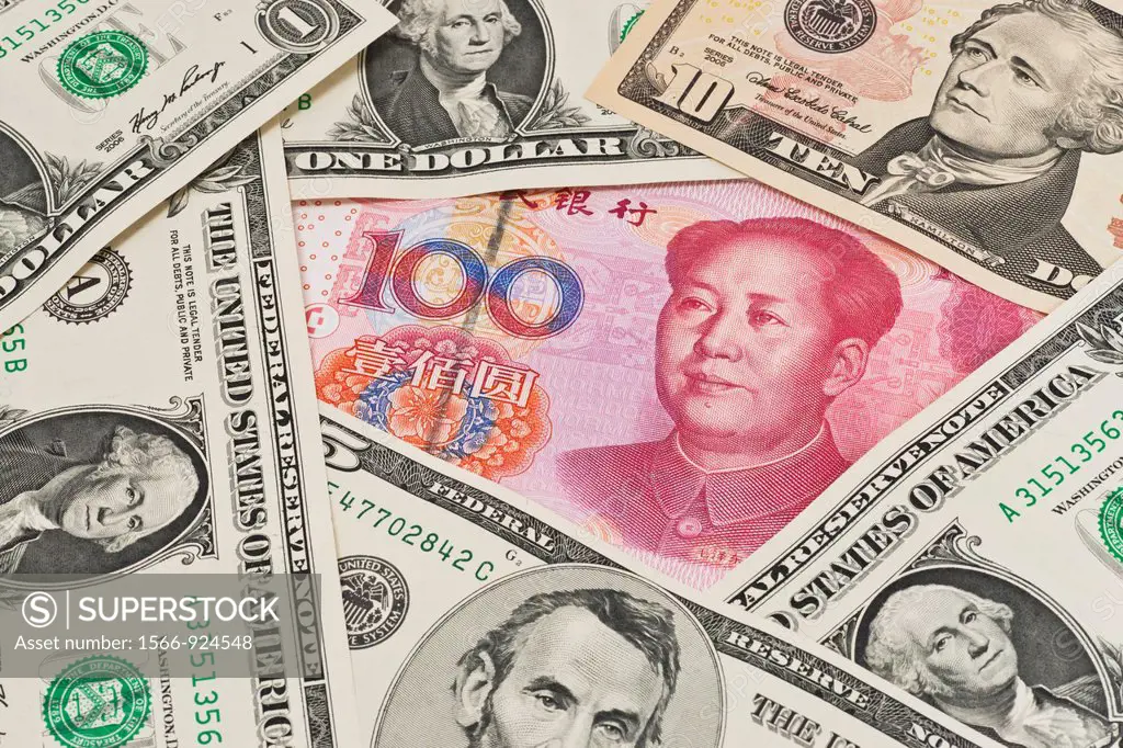 Many U S Dollar bills lying side by side In the middle lies a Chinese 100 Yuan bill with the portrait of Mao Zedong The renminbi, the Chinese currency...