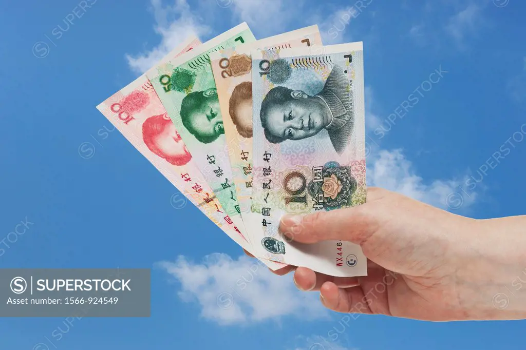 Diverse Chinese Yuan bills with the portrait of Mao Zedong are held in the hand Sky is in the background.