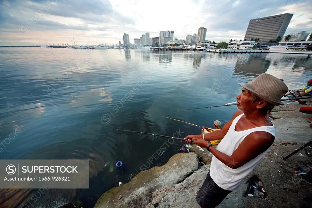 elderly man fishing at the marina in front of the manila skyline, Manila, Philippines, Asia