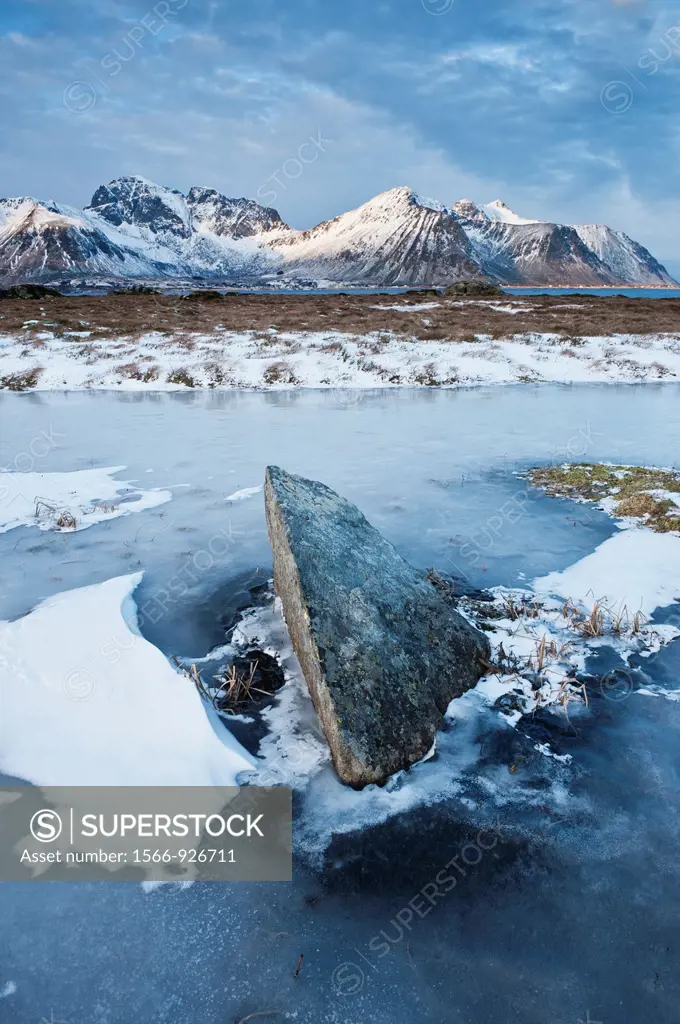 Rock emerges from frozen pond in winter, Lofoten Islands, Norway