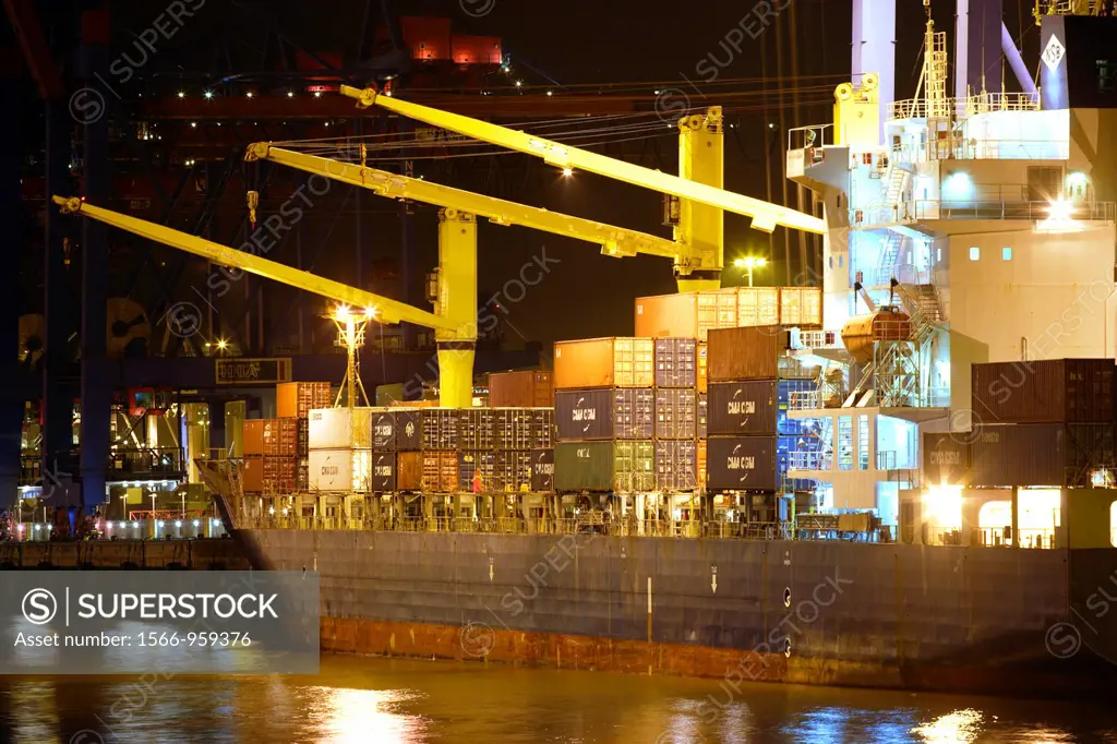 Container ship moored at the container terminal with several cranes offloading container boxes, and river Elbe in the foregound, harbor of Hamburg, Ge...
