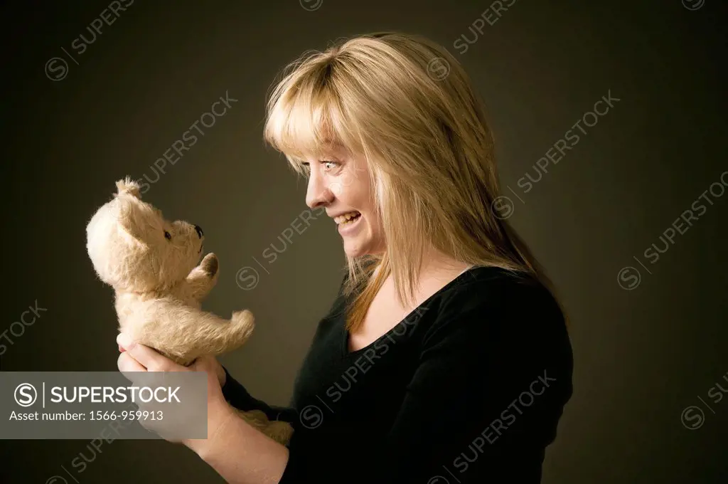 a blonde haired teenage girl woman pulling a face and playing with her old battered teddy bear