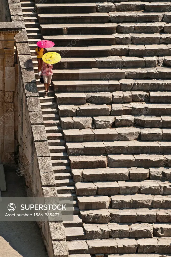 Two tourists descending the steps at the Classical Greek theatre at Ancient Epidaurus, Argolid, Peloponnese, Greece