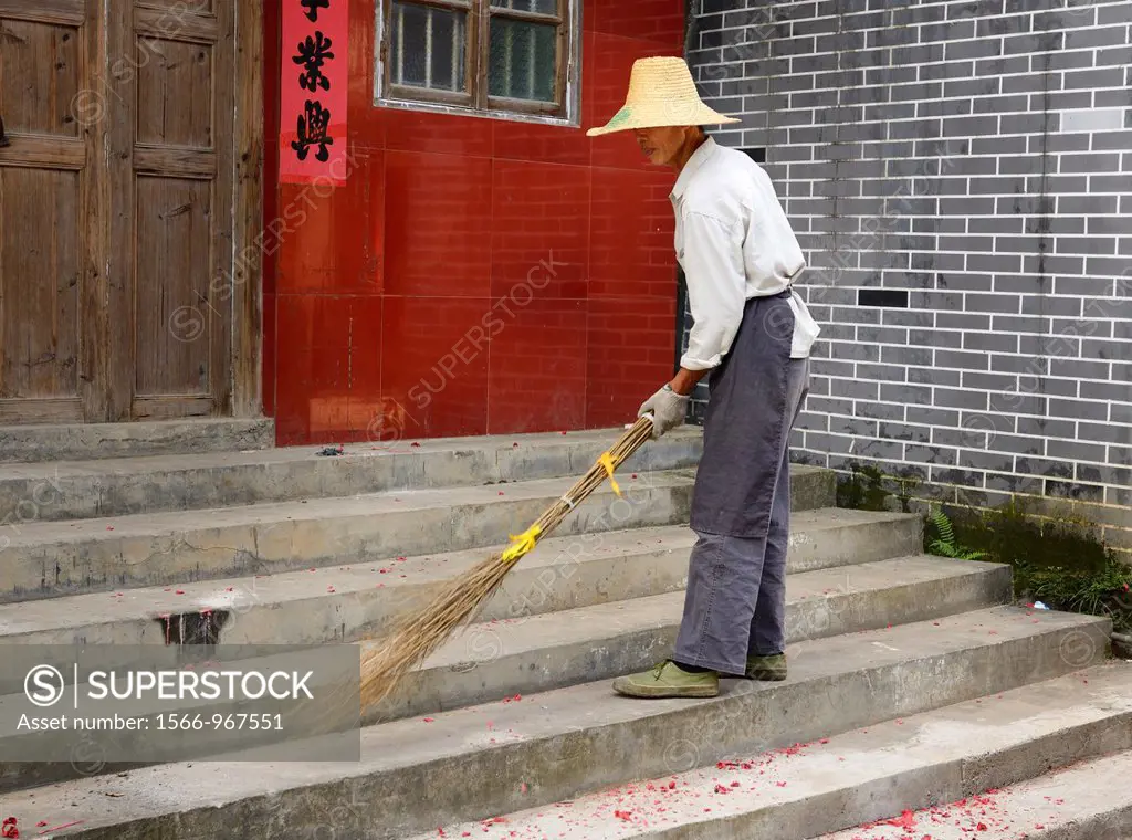Street sweeper cleaning up red fireworks paper with a home made broom in Fuli near Yangshuo China