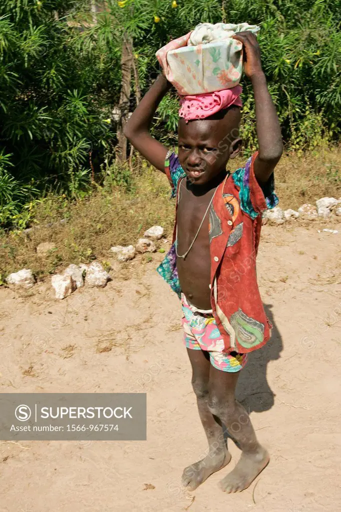 Small barefoot boy carries bowl on head Berending village south of The Gambia