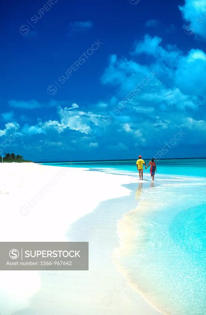 Man and woman stroll hand in hand along idyllic beach Barbuda Caribbean