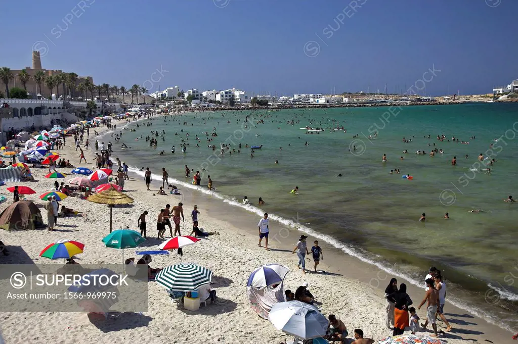 Coloured umbrellas dot beach at Monastir with fort and palms backdrop Tunisia
