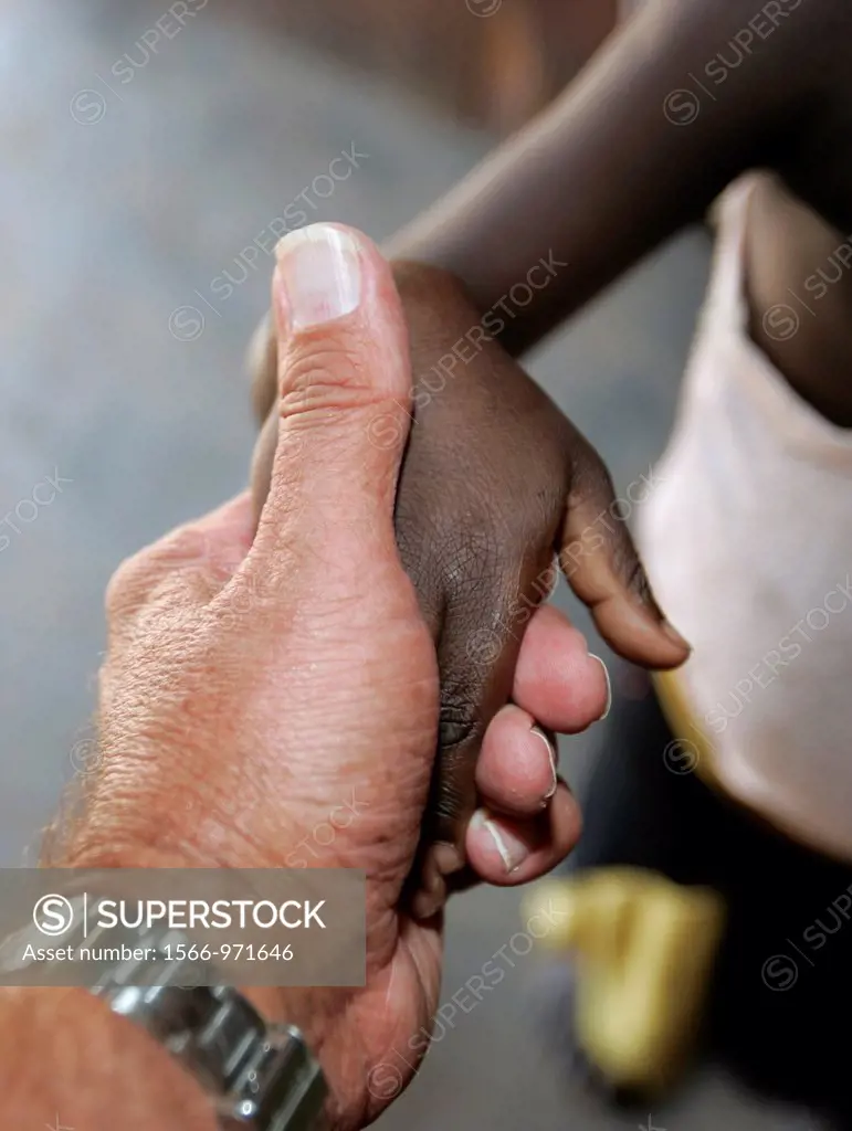 White adult hand holds black child hand Berending village south of The Gambia