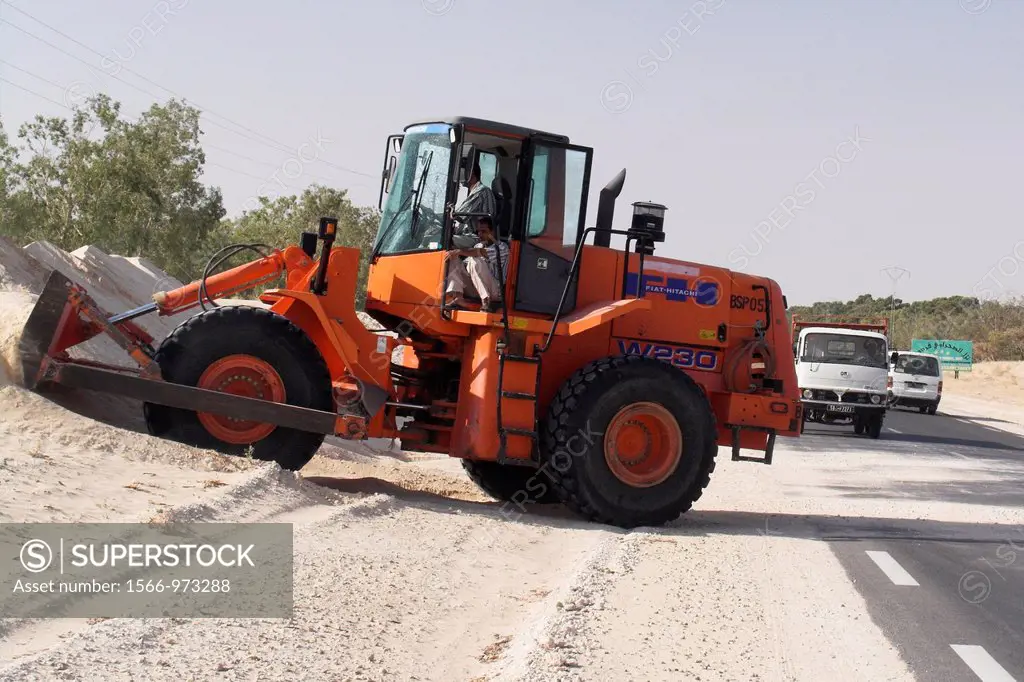 Tractor clears drifting Sahara sands from a main road halting traffic Tunisia
