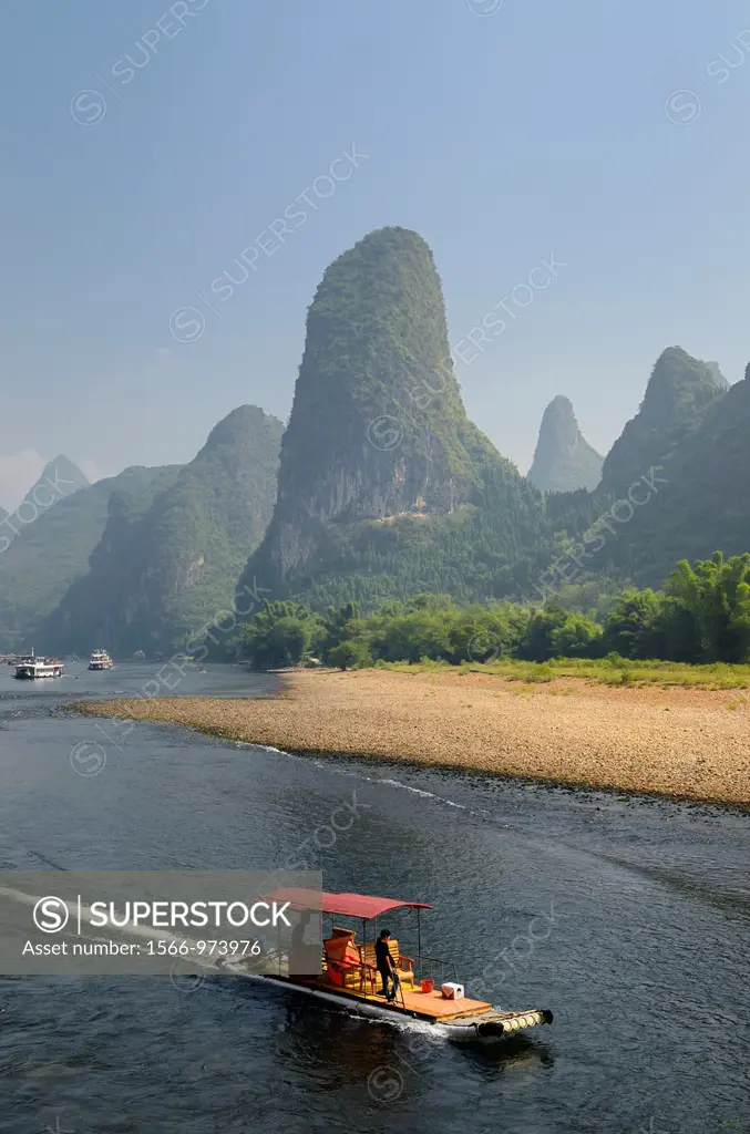 Tour boat raft traveling down the Li river with tall karst mountain cones in background. Guangxi, China.