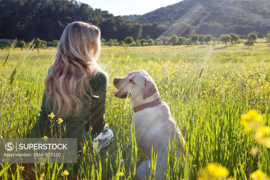 Forty something year old woman sitting in a meadow with her dog