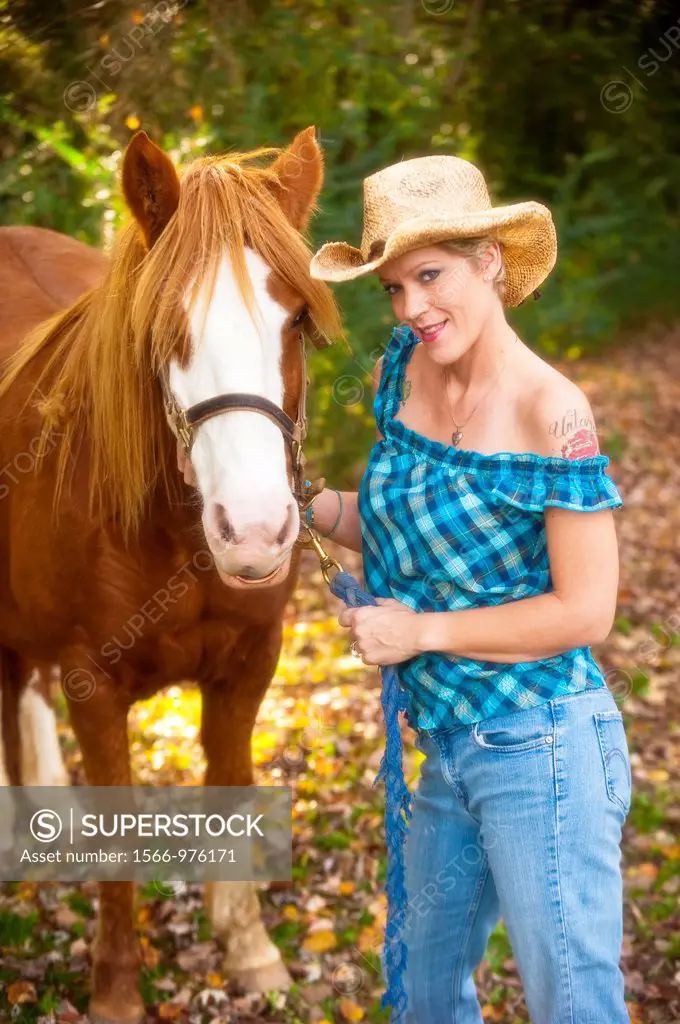 Portrait of a 41 year old blond woman wearing blue jeans walking with a horse in a country setting