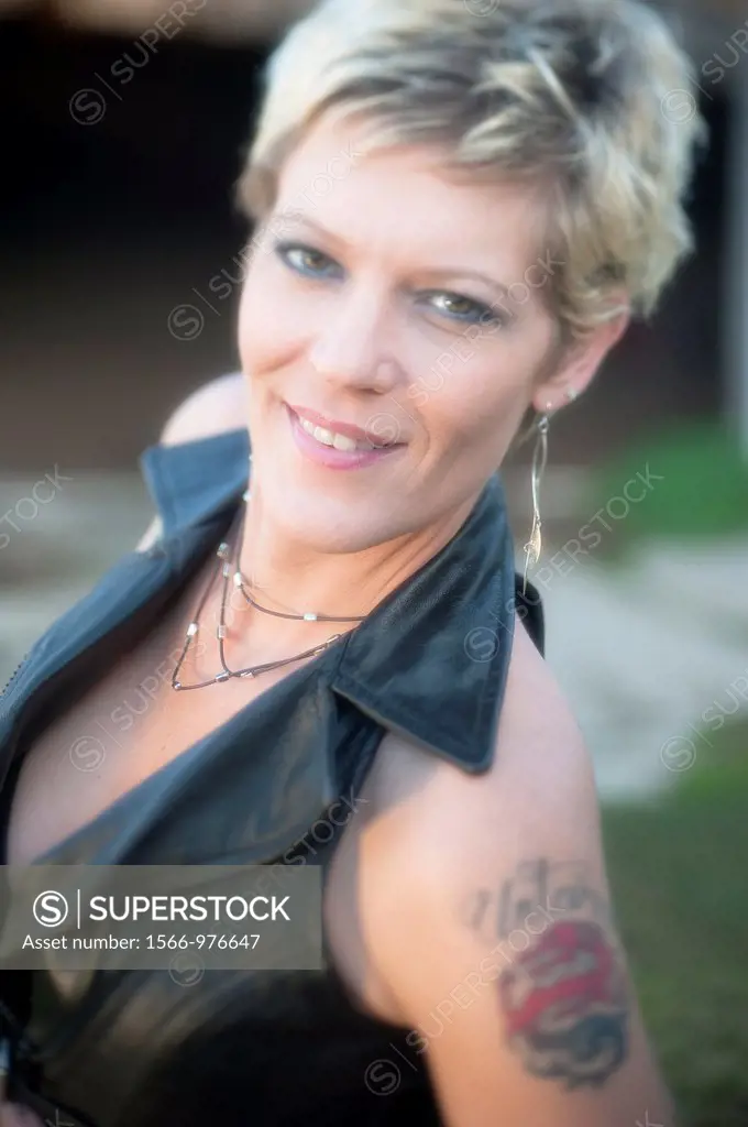 Portrait of a 41 year old blond woman smiling at the camera, tattoo on shoulder
