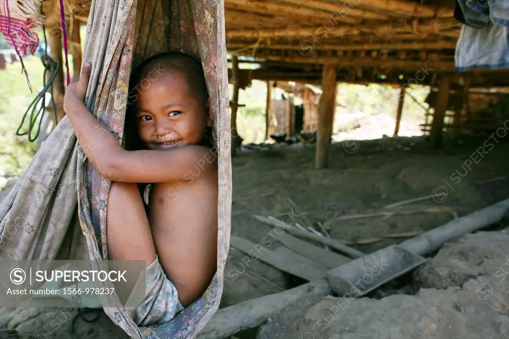Closeup of Burmese boy sitting in a hammock tied to a hut in the displaced persons camp near Thailand In Myanmar Burma, thousands of people have settl...