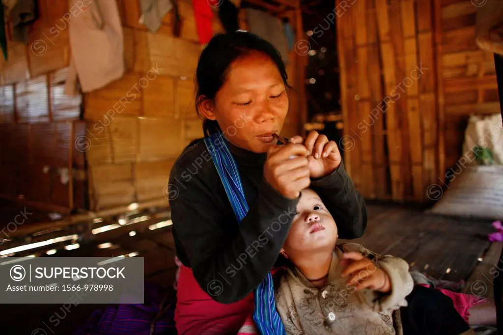 A Burmese mother lights her pipe in her hut while her baby watches In Myanmar Burma, thousands of people have settled near the border as a result of o...