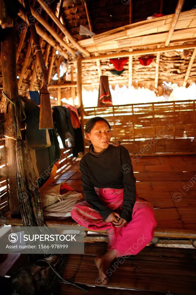 A Burmese woman smoking a pipe in her hut in La Per Her In Myanmar Burma, thousands of people have settled near the border as a result of oppression i...