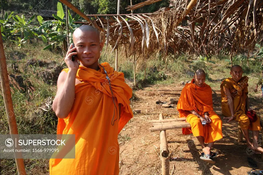 Buddhist monk on the phone with other monks in the background at Mae Sot refugee camp Around 130,000 Burmese refugees have settled in Thailand due to ...