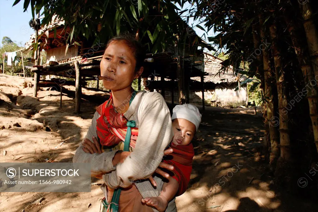 A Burmese woman carrying a baby stands in front of a hut in the village for displaced people In Myanmar Burma, thousands of people have settled near t...