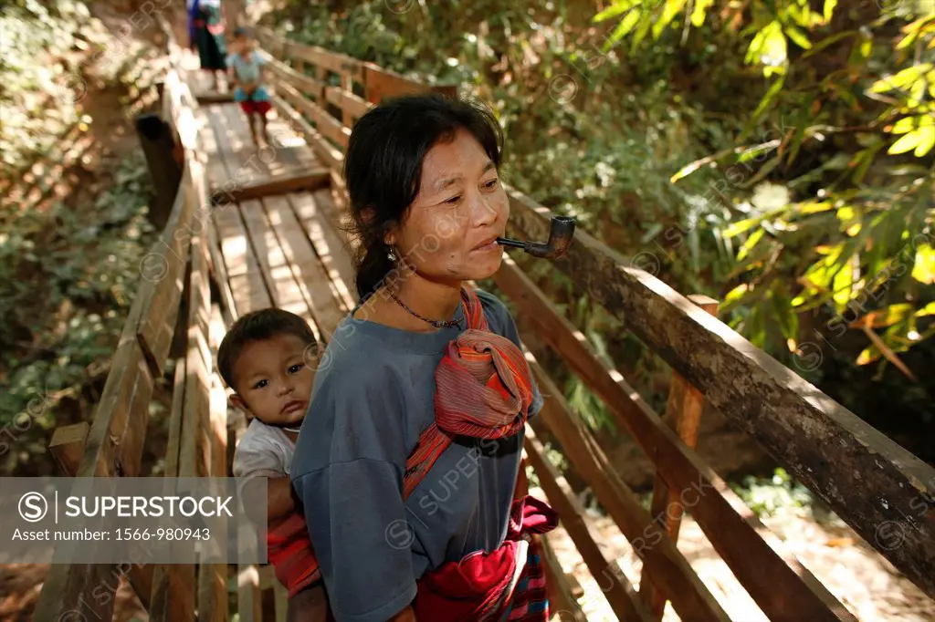 A burmese woman, smoking a pipe, crosses a footbridge with a baby on her back In Myanmar Burma, thousands of people have settled near the border as a ...