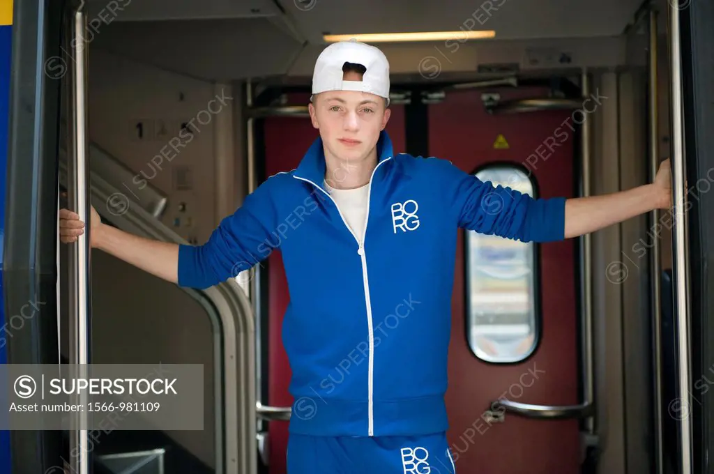 Young man with cap and training-suit, waiting between the doors of a train before departure.