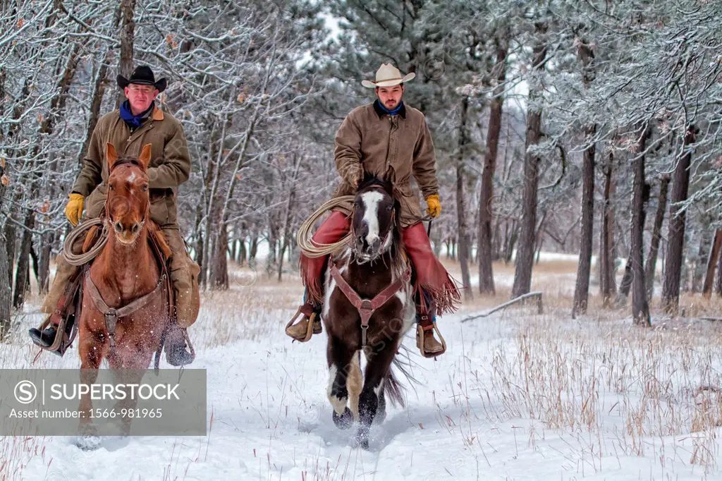 Two cowboys riding horses in the snow