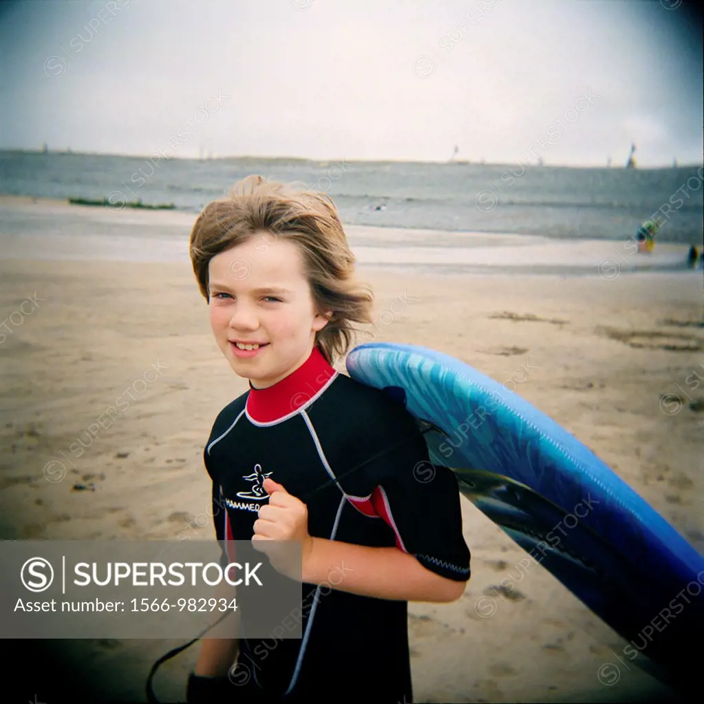 10 year old boy carrying a body-board on the beach at Westward Ho!, Devon, England  Taken with a Holga medium format toy camera