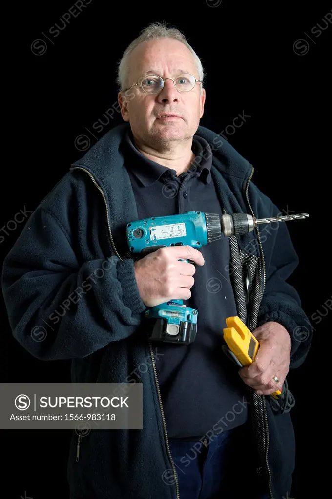 Portrait of an electrician, with his drill and other tools, in front of a black background. Photograph - portrait taken during the reconstruction of a...