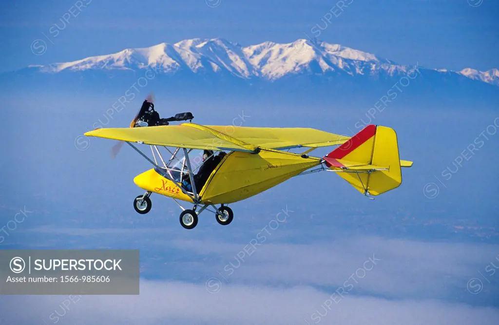 Ultra light plane flying in wintertime over thin clouds around Torreilles  At background the snowed Canigou peak 2784 m  Eastern Pyrenees, Languedoc R...