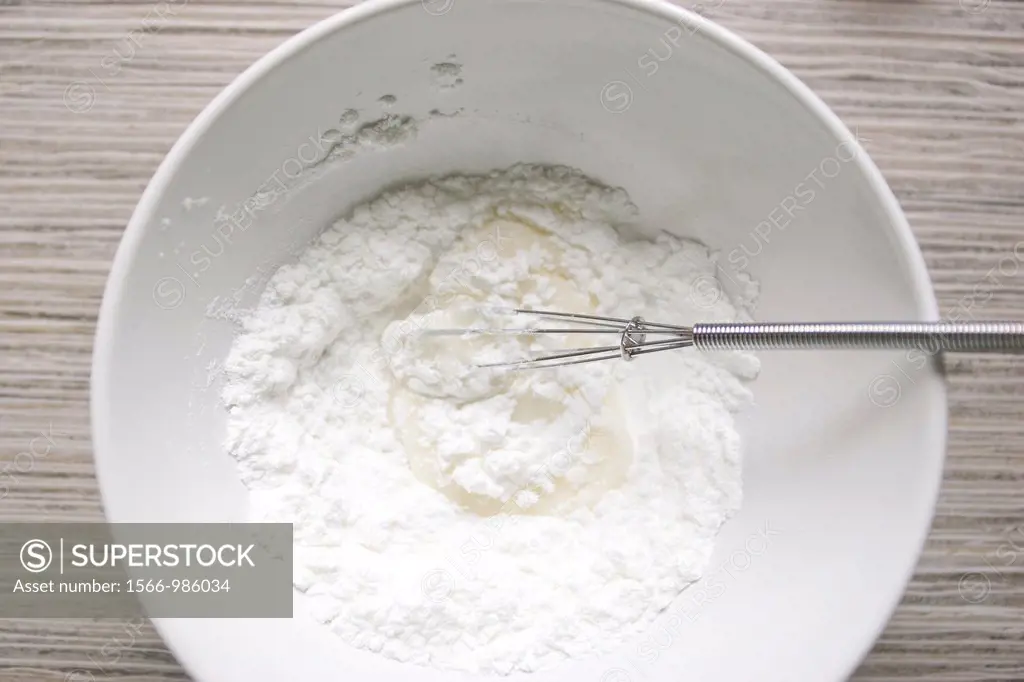 Fluffy white icing sugar and water being mixed with a small whisk