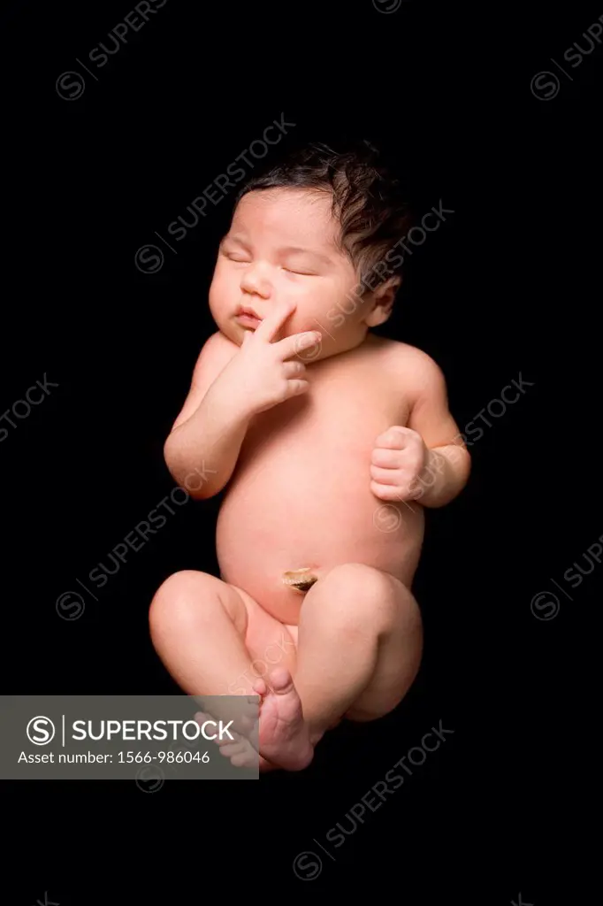 A newborn baby lies sleeping on a black backdrop  Close up